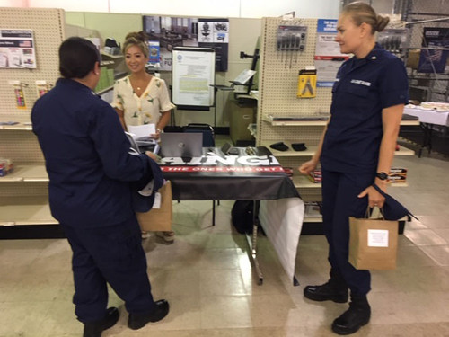 a man and woman in coast guard uniforms standing near a table of products talking to a sales person.
